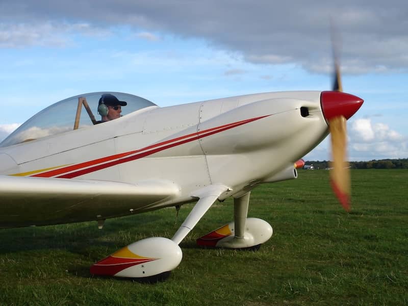 An assembled airplane with a white body and red stripe on a grassy field ready for takeoff.
