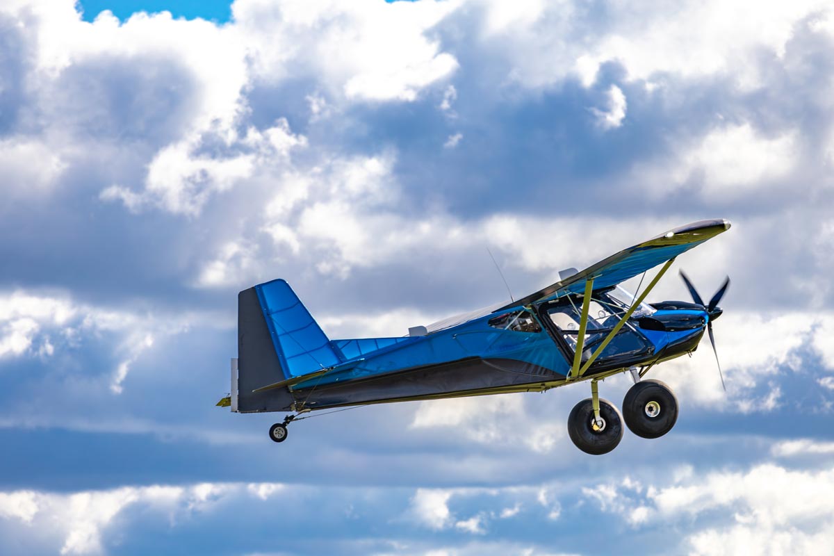 A homebuilt aircraft flies through the sky on a sunny day.